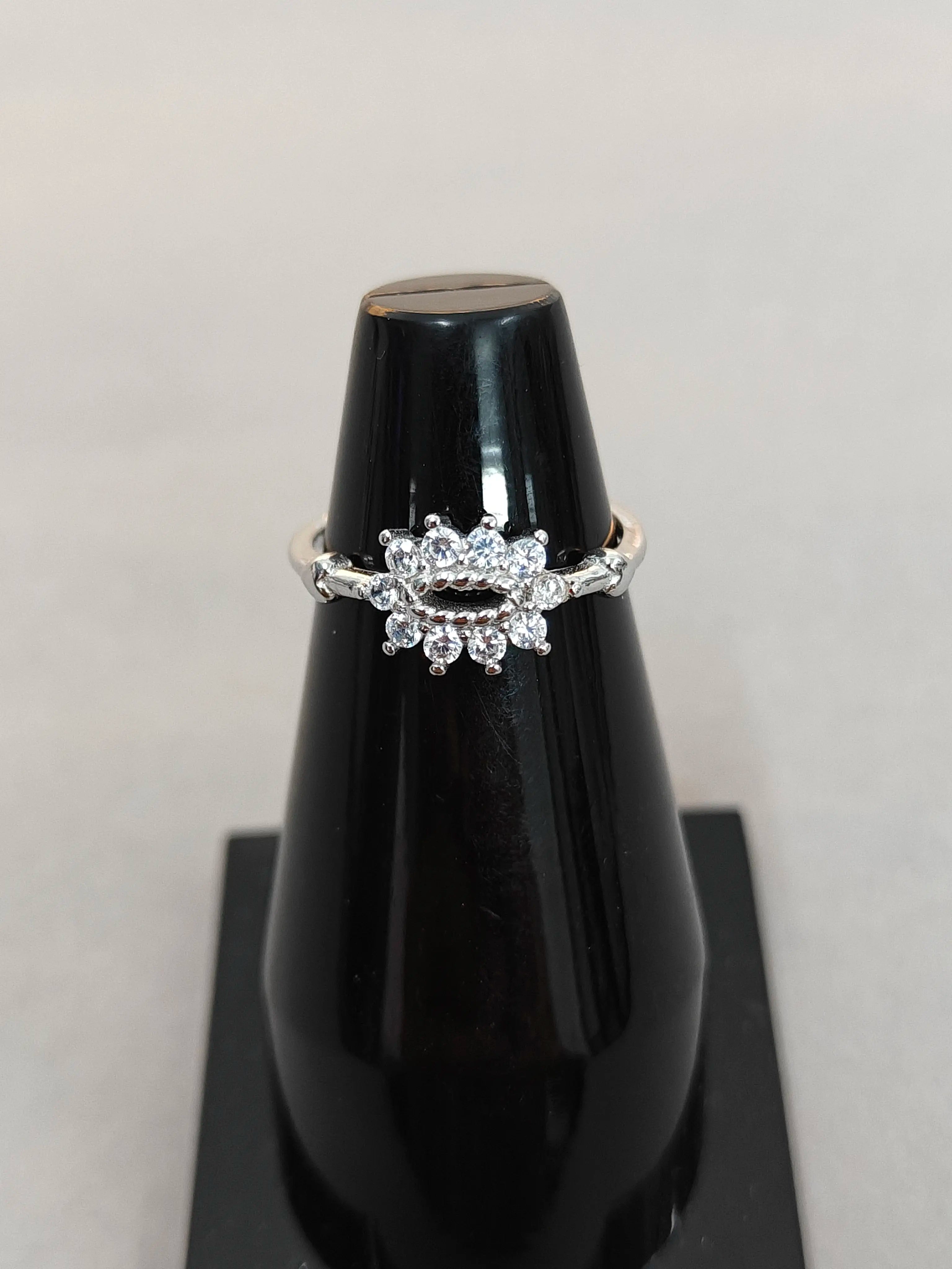 Silver ring with diamonds on a black stand against a light gray background